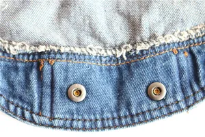 Close-up detail of denim pet vest showing metal snap buttons and frayed edge