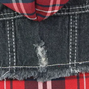 Close-up detail of distressed denim texture and red plaid stitching on a pet vest garment