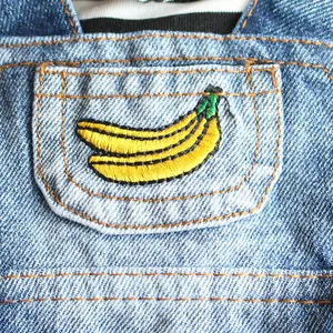 Macro detail of a yellow embroidered banana on a classic denim pet dress front pocket