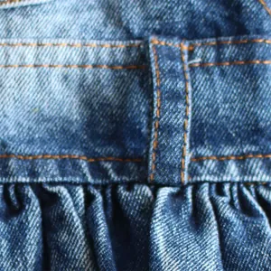 Close-up of blue denim fabric with orange stitching and pleated texture for pet dress