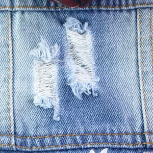 Close-up detail of blue ripped denim pet vest with yellow stitching and daisy embroidery.
