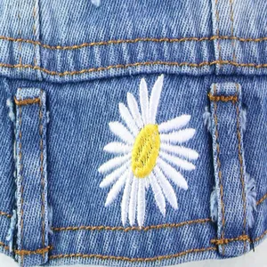 Detailed close-up showing white daisy embroidery on light blue denim dog vest garment