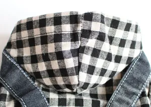 Nahaufnahme des schwarz-weißen Gingham-Stoffs und des Denim-Trägers eines Haustierkleides im Detail.