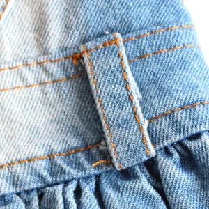 Close-up macro view of blue denim pet dress fabric with orange contrast stitching details