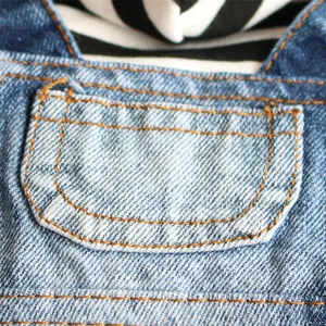 Gros plan de vêtements en denim bleu pour animaux avec poche et coutures orange.