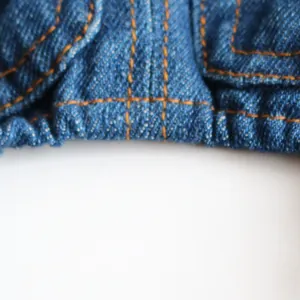 Macro detail of blue denim pet clothes featuring orange contrast stitching and elastic hem