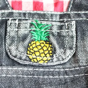 Detail view of yellow pineapple embroidery on a dark wash denim pet dress pocket