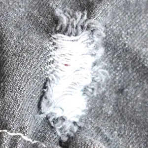 Detailed macro view showing the distressed frayed denim fabric of pet jumpsuit garment