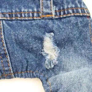 Detailed view of the distressed hole and orange stitching on a blue dog denim jumpsuit