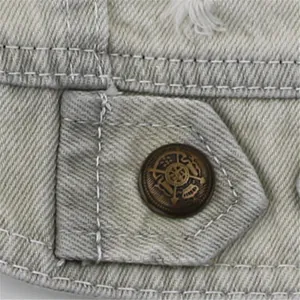 Macro detail of the metallic button and white stitching on a grey distressed pet denim vest