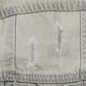 Close-up detail of ripped distressed denim fabric on a pet vest with white stitching