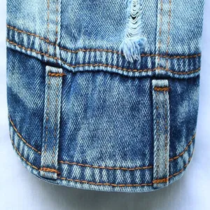 Gedetailleerde macro-opname van blauwe denim hondenharnasvest met oranje stiksels en textuur