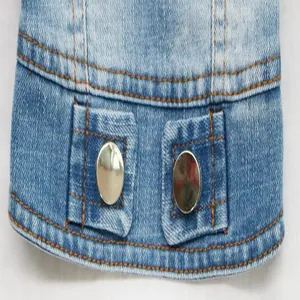 Close-up of blue denim pet vest showing metallic buttons and orange stitching detail.