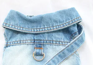 Macro detail of denim pet clothing showing reinforced metal D-ring and orange stitching