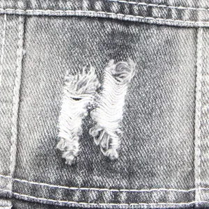 Gros plan du trou déchiré en forme de N sur la texture du gilet en denim noir pour animaux