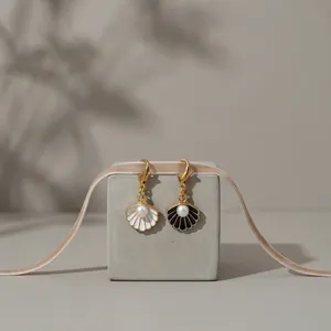 Detailweergave van wit en zwart emaille schelphangers met parels en gouden karabijnsluiting
