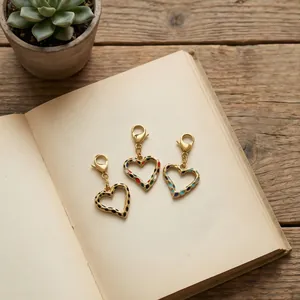 Detailopname van drie kleurrijke hartvormige bedeltjes met gouden karabijnsluitingen.