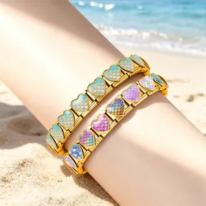 Detailansicht goldener Herz-Modulararmbänder mit bunten Meerjungfrauenschuppen am Strand.