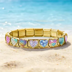 Nahaufnahme von herzförmigen Armbandgliedern mit Meerjungfrauen-Schuppen auf feinem Sand.