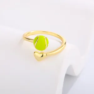 Macro detail of a gold adjustable ring featuring a bright neon tennis ball and a heart