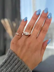 Close-up detail of a rose gold marquise diamond ring set on a hand with blue nails.