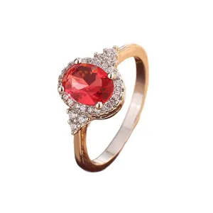 Elegant oval red imitation ruby ring with a sparkling diamond halo in gold tone.