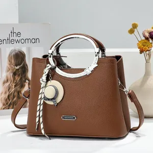 Detail of brown lychee pattern handbag with circular metal handles and hat charm