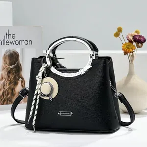 Close-up of black lychee texture handbag featuring a silver round handle and hat charm.