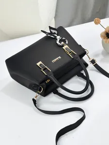 Detail van een elegante zwarte handtas met gouden logo en zijden sjaalaccessoire