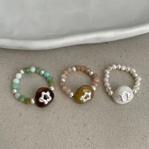 Detailed view of three handmade natural stone and pearl elastic rings with flowers.