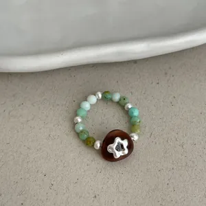 Detailed close-up of a handmade beaded elastic ring with green stones and a pearl