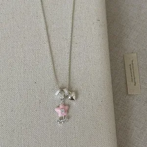 Close-up of sweet pink enamel flower pendant necklace with a small silver heart charm.