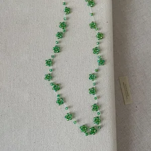 Gedetailleerd overzicht van handgemaakte groene kralen bloem ketting op beige textuur
