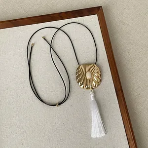 Close-up of minimalist gold shell pendant with white tassel on black cord necklace