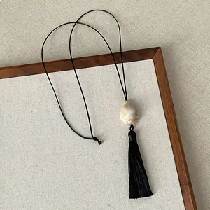 Detailed view of a Zen style black tassel necklace featuring a cream-colored stone pendant.