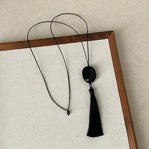 Detailed view of a black Zen-style tassel necklace on a textured linen display tray