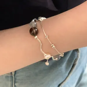 Vista detallada de una pulsera elástica con piedras naturales y perla en la muñeca.