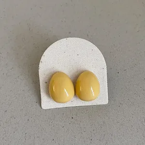 Close-up of vibrant yellow glossy bean-shaped stud earrings displayed on white card