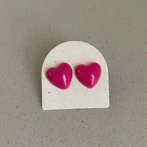 Close-up of vibrant magenta drip oil heart stud earrings on a textured display card