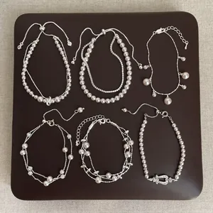 Set of six elegant pearl and silver chain bracelets displayed on a brown textured pad
