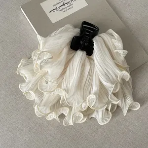 Macro view of a white ruffled fabric hair claw clip with elegant pleated texture design