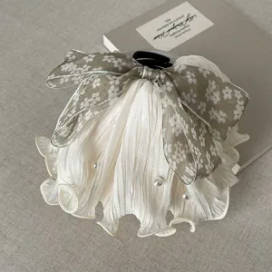 Detailed view of a floral bow hair claw clip with pleated fabric and pearl accents.