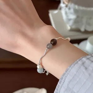 Detalle de una pulsera de metal ondulado con cuentas de piedra natural y dije de estrella