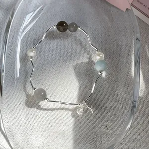 Primer plano de una pulsera minimalista con piedras naturales, perlas y dijes de estrella de mar