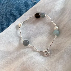 Elegante primer plano de dijes de estrella de mar y concha en una pulsera de piedras naturales