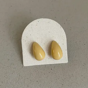 Close-up detail of glossy yellow teardrop bean stud earrings on white textured card display