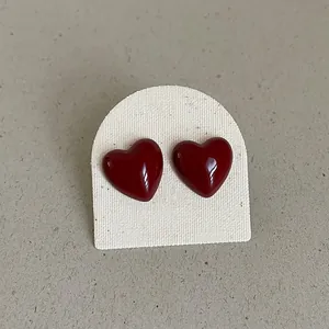 Detail view of glossy dark red heart shaped stud earrings with a smooth enamel finish