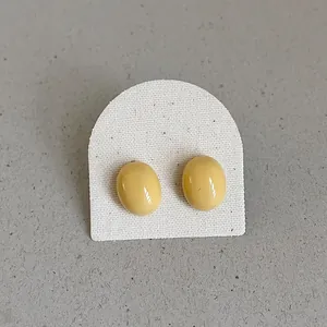 Close-up of smooth pale yellow bean-shaped stud earrings on a display card