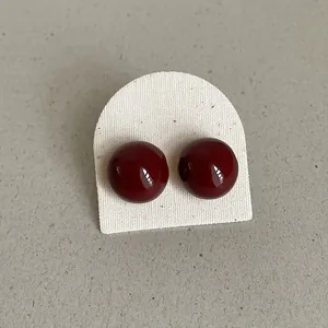 Close-up of glossy burgundy round bean stud earrings on a white textured display card holder