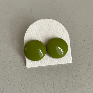 Close-up of glossy olive green bean-shaped stud earrings on a textured white card